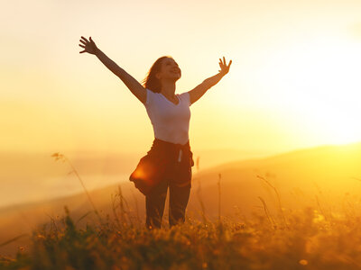 Frau streckt Arme der Sonne entgegen, um achtsam Dankbarkeit, Licht und Liebe zu genießen
