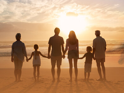 Mehrere Generationen einer Familie betrachten Sonnenuntergang am Strand und spüren Kraft der Ahnen